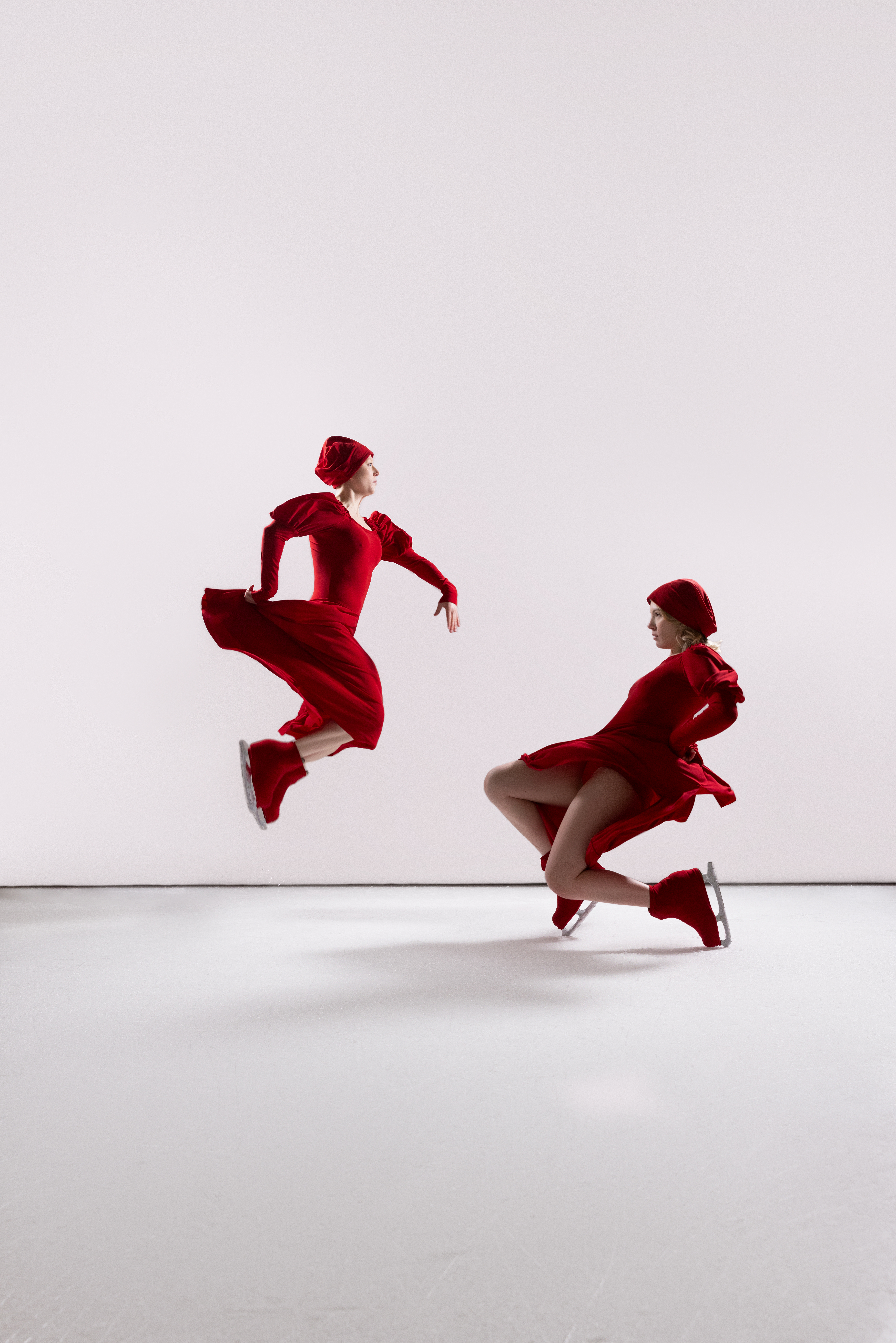 Two figure skaters in red garments, mid-air, mirrored movement